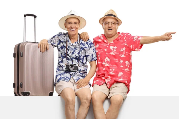 Turisti di sesso maschile anziani seduti su un pannello con una valigia e un perno — Foto Stock