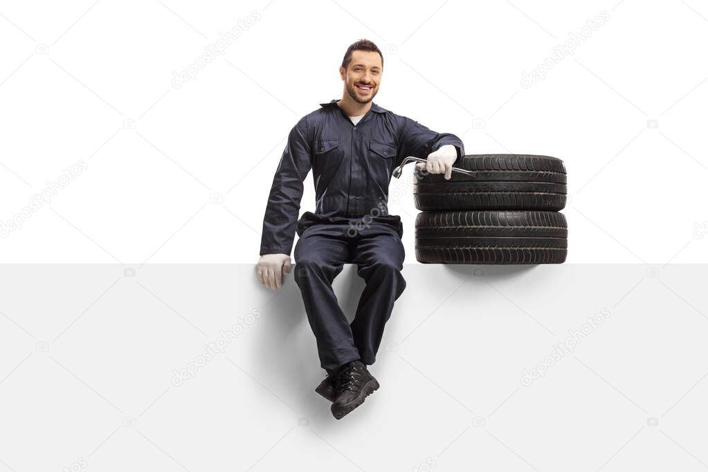 Auto mechanic sitting on a panel with tires and a wrench 