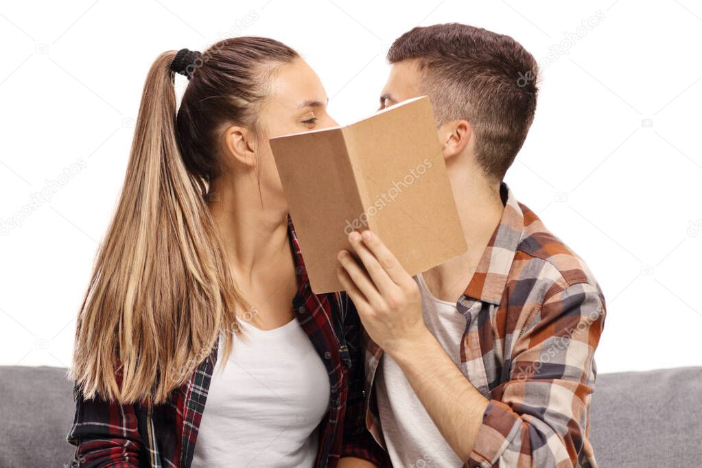 Boy and girl kissing and hiding behind a book