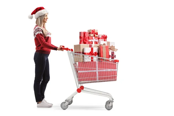 Young woman with a santa claus hat pushing a shopping cart with — Stock Photo, Image