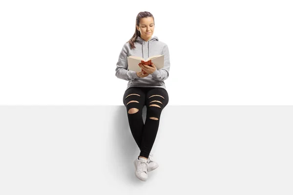 Young female reading a book and sitting on a banner — Stock Photo, Image