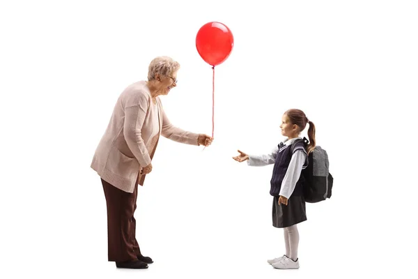 Senior woman giving red balloon to a schoolgirl — Stock Photo, Image