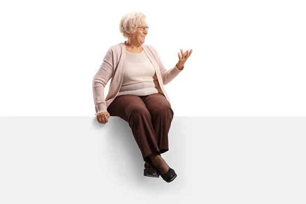 Femme âgée assise sur un panneau regardant vers le côté et gesturi — Photo
