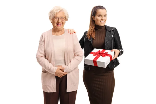 Egy fiatal nő ajándékot tart, és egy idősebb hölgy mellett pózol. — Stock Fotó