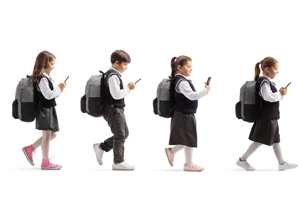 Tres colegialas y un colegial con teléfonos móviles caminando i —  Fotos de Stock