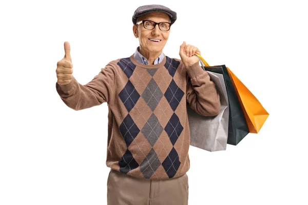 Yaşlı bir adam baş parmağını gösteriyor ve alışveriş torbaları taşıyor. — Stok fotoğraf