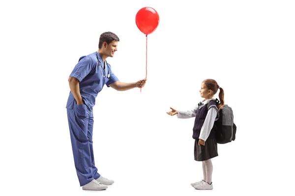 Arzt in blauer Uniform überreicht einem kleinen Schulmädchen einen Luftballon — Stockfoto