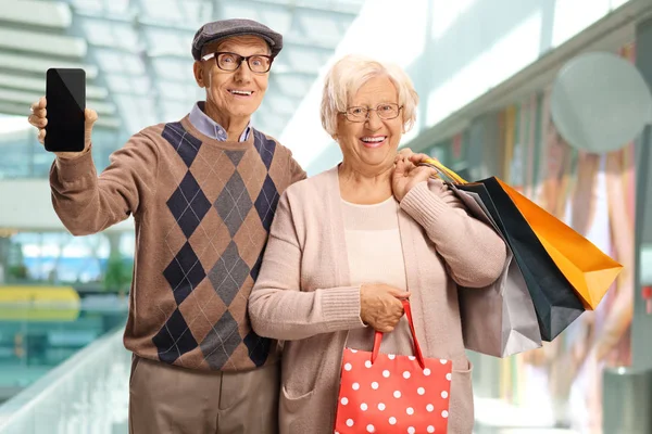 Oudere man en vrouw in een winkelcentrum met mobiele telefoon en winkelpin — Stockfoto