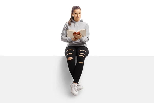 Joven hembra sentada en un panel y leyendo un libro — Foto de Stock