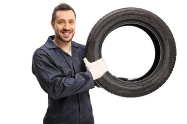 Araba tamircisi araba lastiği tutuyor ve kameraya gülümsüyor. 