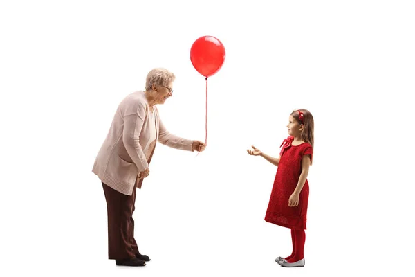 Grandmother giving a red balloon to a girl in a red dress — Stock Photo, Image