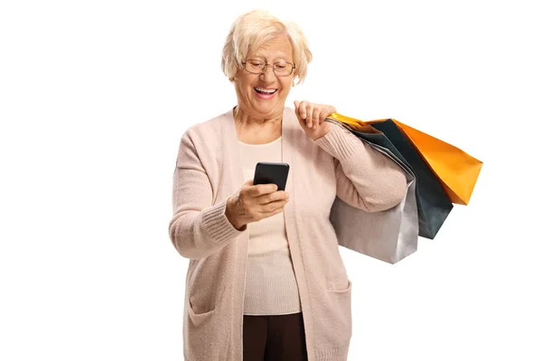 Alışveriş torbaları taşıyan ve cep telefonuna bakan yaşlı bir kadın. — Stok fotoğraf