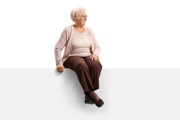 Femme âgée assise sur un panneau vierge et regardant vers le côté — Photo