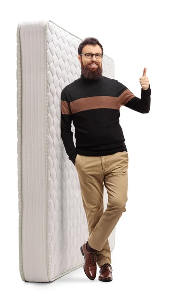 Bearded guy showing thumbs up and leaning on a mattress — Stockfoto