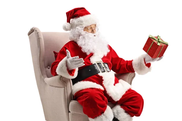 Święty Mikołaj siedzi w fotelu i trzyma pudełko z prezentami — Zdjęcie stockowe