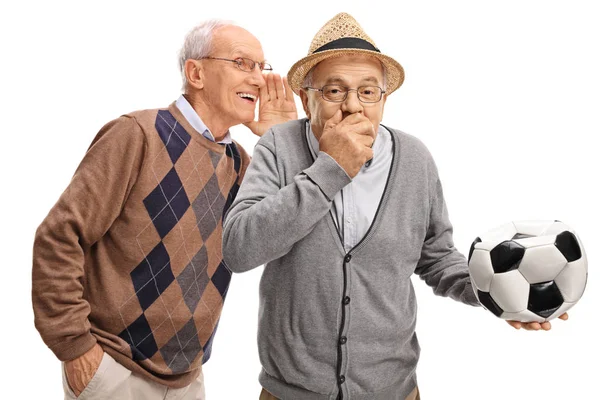 Senior man whispering to friend holding a deflated soccer ball a — Stock Photo, Image