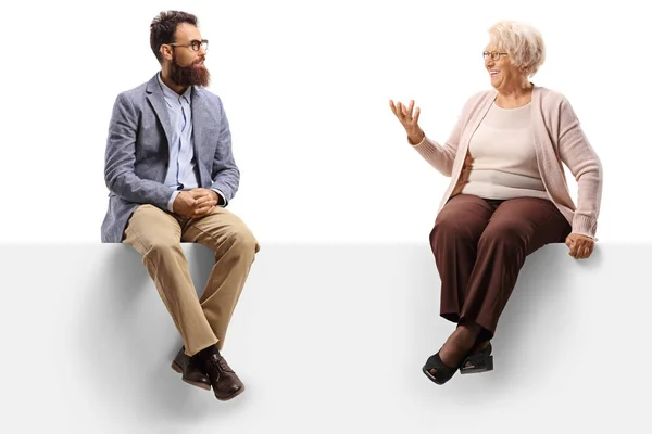 Senior lady sitting on a blank panel and talking to a younger be — Stock Photo, Image