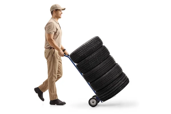Entrega homem empurrando um caminhão de mão carregado com pneus de carro — Fotografia de Stock