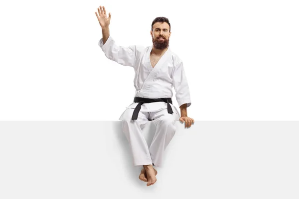 Uomo karate barbuto in kimono con cintura nera seduta su un pannello — Foto Stock