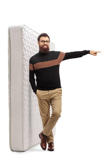 Hombre barbudo apoyado en un colchón de cama y apuntando hacia un lado —  Fotos de Stock