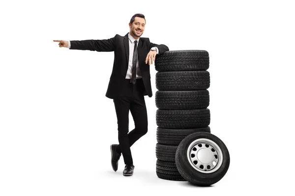 Man wearing a black suit, leaning on car tires and pointing to o — Stock Photo, Image