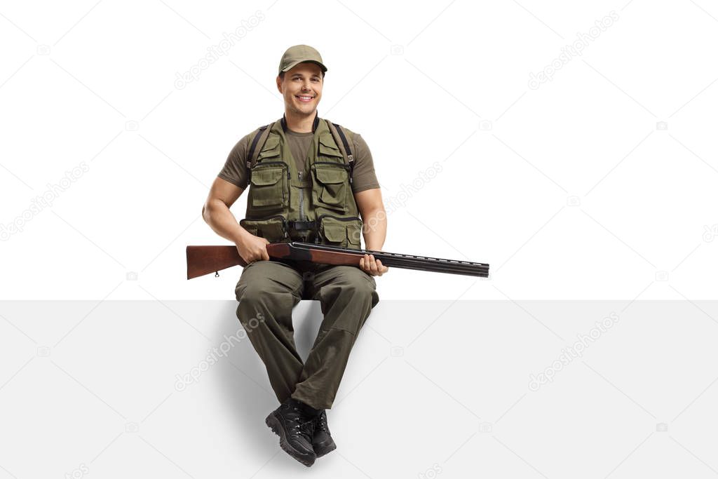 Young man hunter with a rifle sitting on a blank board