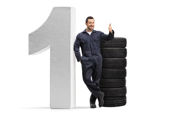 Mecánico posando con una pila de neumáticos de coche y un gran número uno, s —  Fotos de Stock