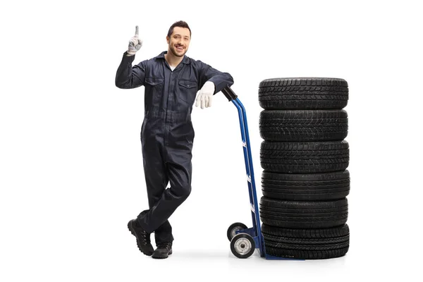 Mecânico com pneus de carro em um caminhão de mão apontando para cima — Fotografia de Stock