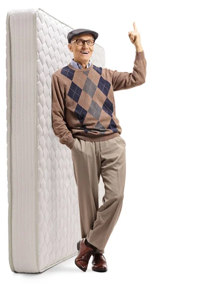 Starszy mężczyzna opierający się o materac i wskazujący powyżej — Zdjęcie stockowe