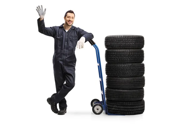 Mechanic with car tires on a hand truck waving — Stock Photo, Image
