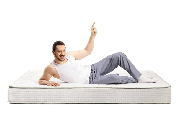 Jongeman liggend op een bed matras in pyjama en wijzend boven — Stockfoto