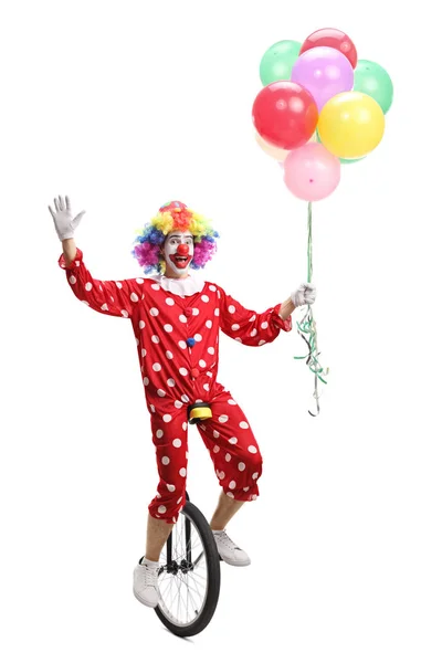 Glücklicher Clown, der auf einem Einrad reitet, einen Haufen Luftballons in der Hand hält und — Stockfoto