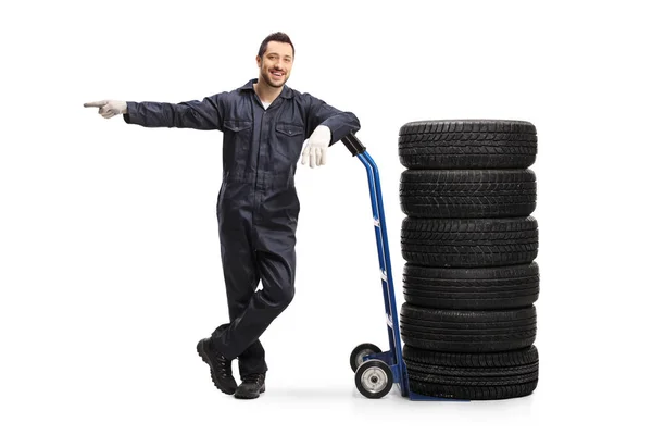 Auto mechanic leaning on a hand truck with tires and pointing — Stock Photo, Image