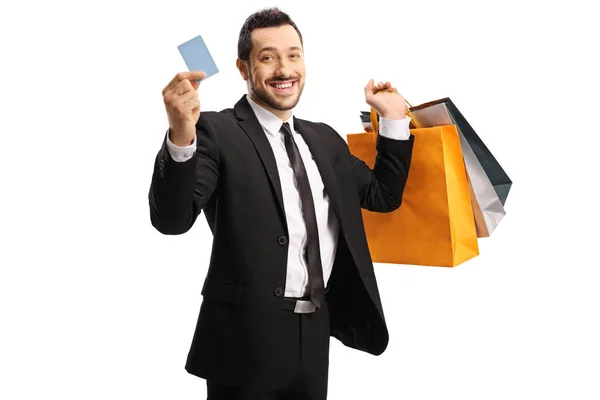 Young man in a suit with shopping bags showing a credit card — Stock Photo, Image