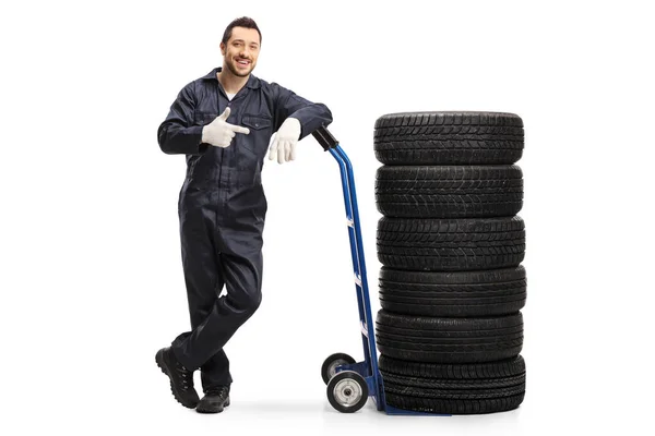 Mechanik samochodowy w mundurze stojący z oponami na wózku — Zdjęcie stockowe