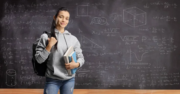 Menina com mochila e livros em pé na frente de um quadro-negro w — Fotografia de Stock