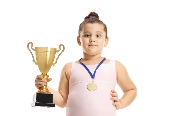Küçük jimnastikçi kız elinde altın bir kupa ve madalya tutuyor. — Stok fotoğraf