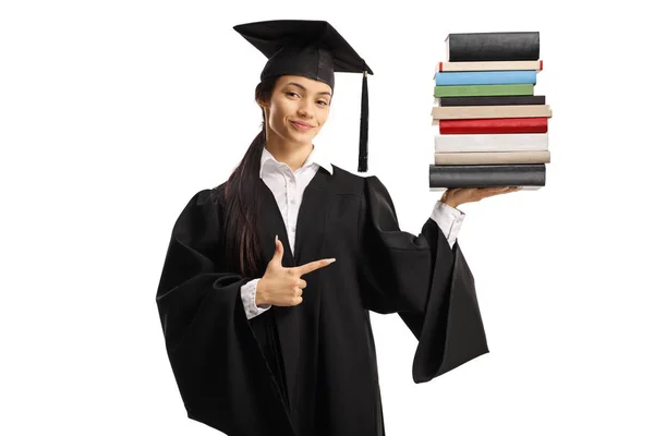 Mujer graduada en un vestido con un montón de libros y señalando —  Fotos de Stock