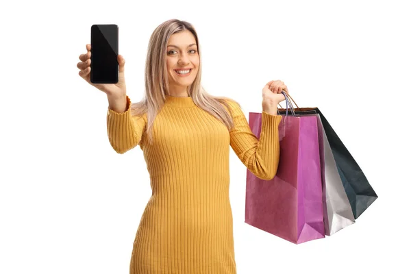 Blond kvinna visar en mobiltelefon och bär shoppingväskor — Stockfoto