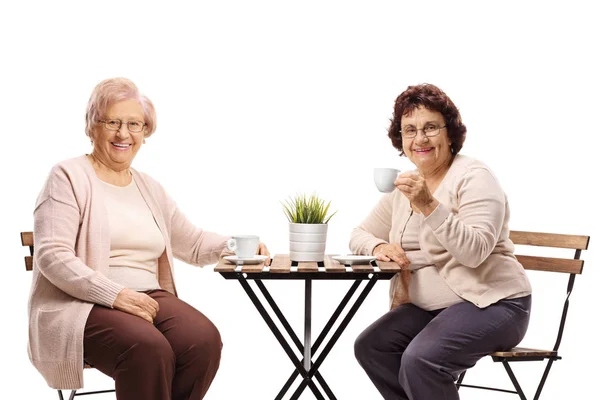 Старшие женщины сидят за столом, пьют кофе и улыбаются — стоковое фото