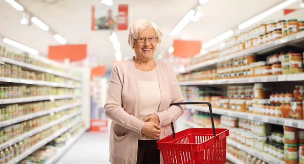 Oudere vrouw met een boodschappenmandje in een supermarkt — Stockfoto