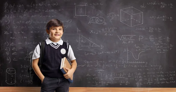 Schüler mit Büchern und Rucksack steht vor einer Tafel — Stockfoto