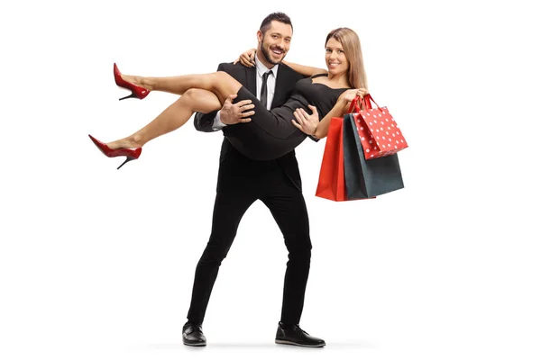Jonge man in een pak draagt een jonge vrouw met boodschappentassen in — Stockfoto