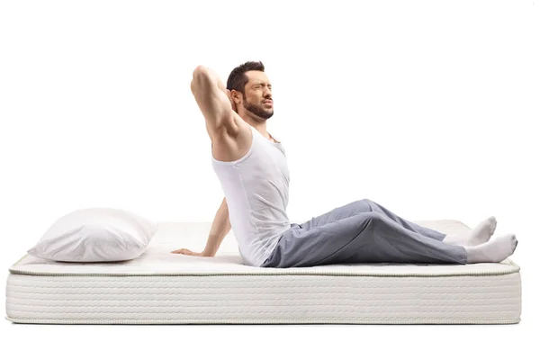 Young man on a bed mattress holding his stiff neck — 스톡 사진