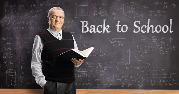 Anciano maestro masculino con la celebración de un libro en frente de una escuela bl —  Fotos de Stock