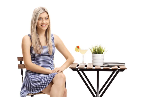 Młoda kobieta siedzi przy stole z koktajlem i patrzy na — Zdjęcie stockowe