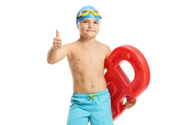 Çocuk elinde bir yüzme tahtası tutuyor ve baş parmağını kaldırıyor. 