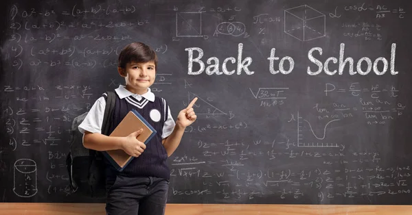 Schooljongen in uniform die boeken vasthoudt en wijst naar een zwijn — Stockfoto