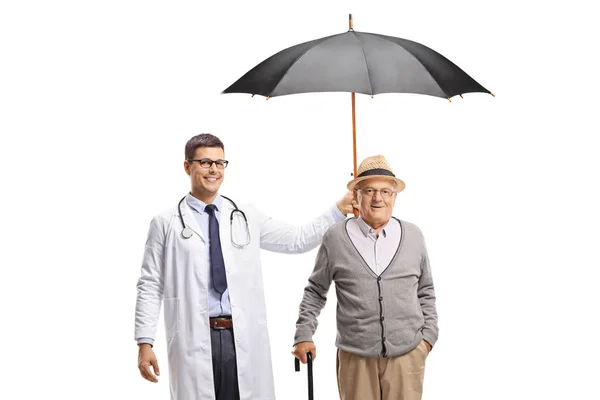 Jovem médico masculino segurando um guarda-chuva sobre um homem idoso — Fotografia de Stock