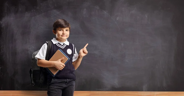 Schoolboy with a book pointing on a blackboard — Stock Photo, Image